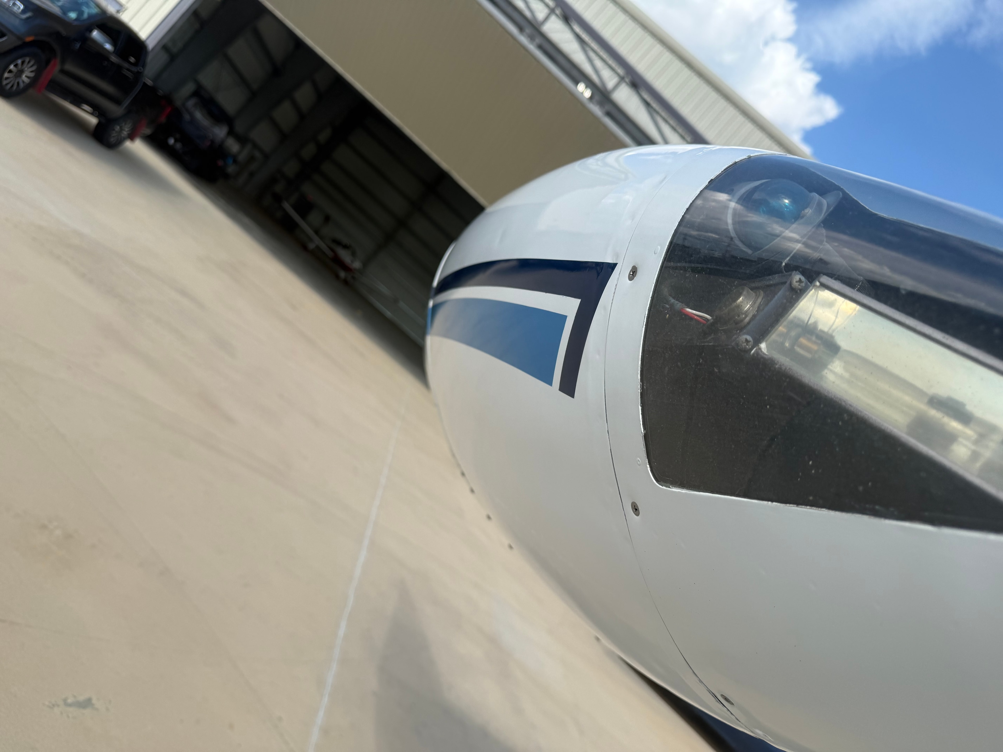 White aircraft nose and cockpit on tarmac outside hangar